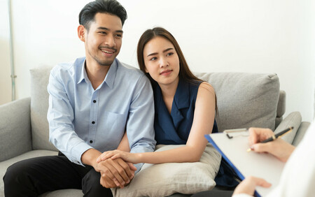 asian couple smiling on couch talking to a doctor